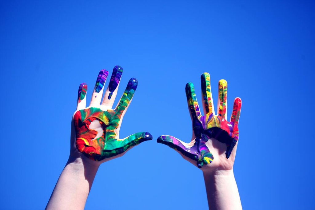 Bunte Hände mit Farbe bemalt vor klarem Himmel.