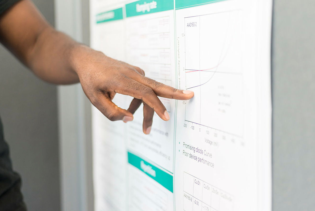 Nahaufnahme einer Hand, die auf ein wissenschaftliches Diagramm auf einem Poster zeigt.
