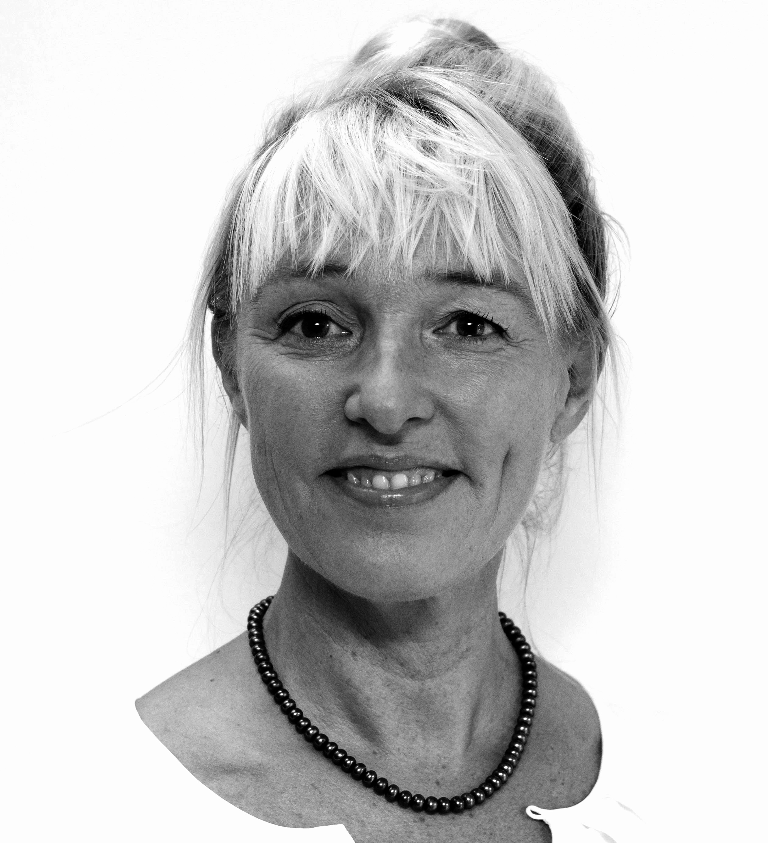Portrait einer älteren Frau mit Hochsteckfrisur und Perlenkette vor weißem Hintergrund.